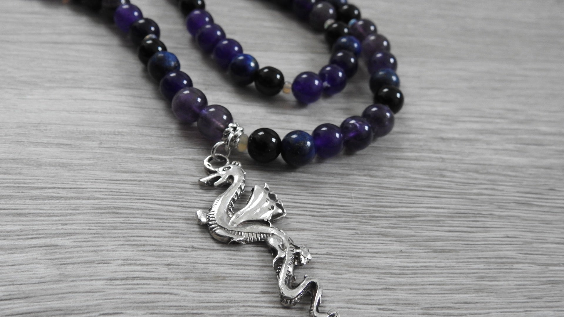 Handcrafted dragon pendant in sterling silver featuring blue lapis lazuli, amethyst, obsidian, and opal stones, front view against white background.