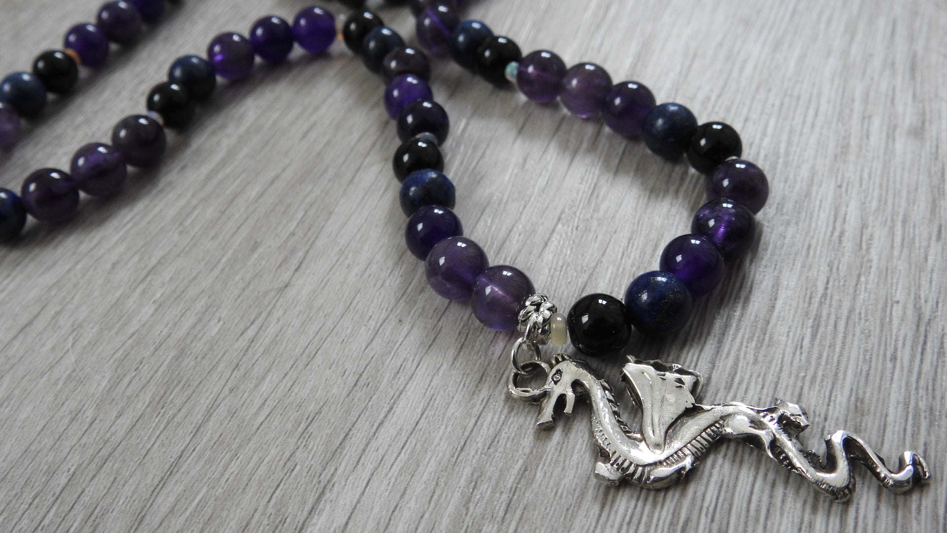 Close-up detail of dragon pendant showing intricate placement of blue lapis lazuli, amethyst, obsidian, and opal semi-precious stones in sterling silver setting.