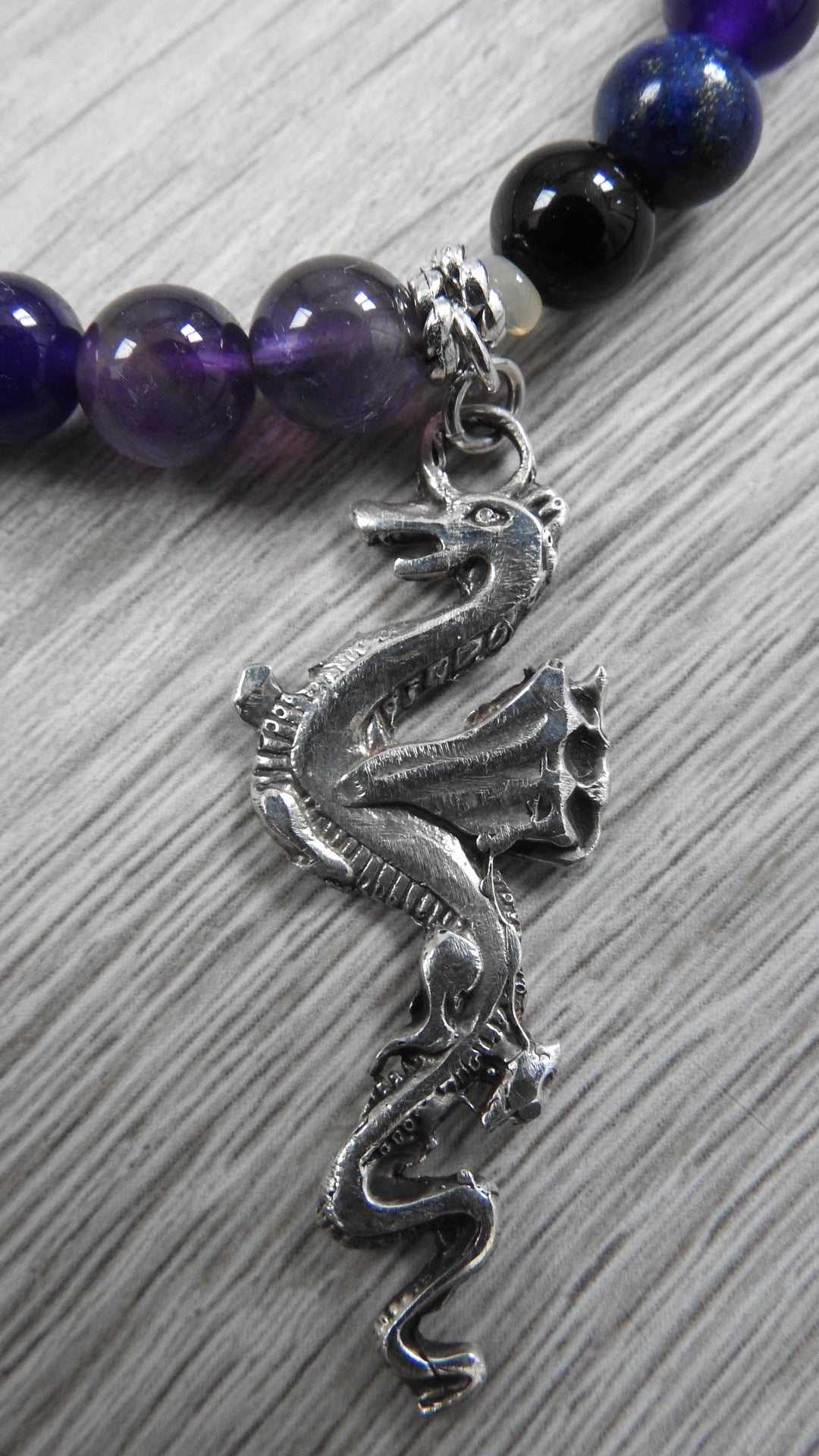 Profile view of handcrafted dragon pendant displaying sterling silver texture work, antique silver accents, and semi-precious stone integration.