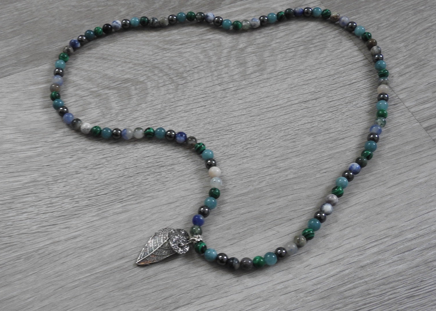 Side profile view of handcrafted sterling silver leaf and coral pendant showing three-dimensional organic form and texture blend.