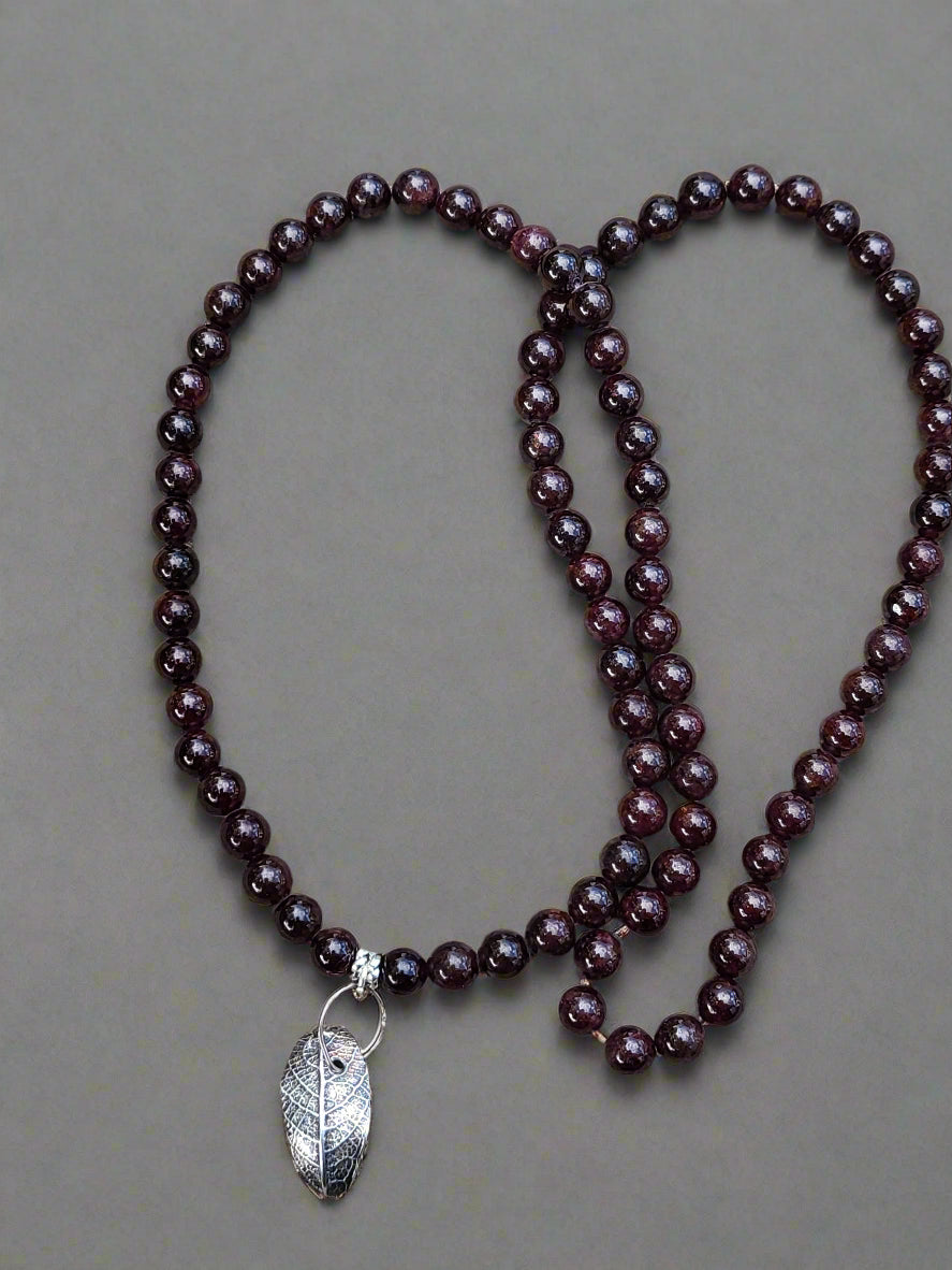 Artistic lifestyle shot of sterling silver leaf necklace with garnet highlighting natural woodland inspiration and memory preservation in silver.