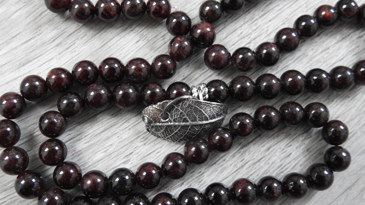 Side profile view of sterling silver leaf pendant showing three-dimensional organic leaf form with garnet accents and antique finish.