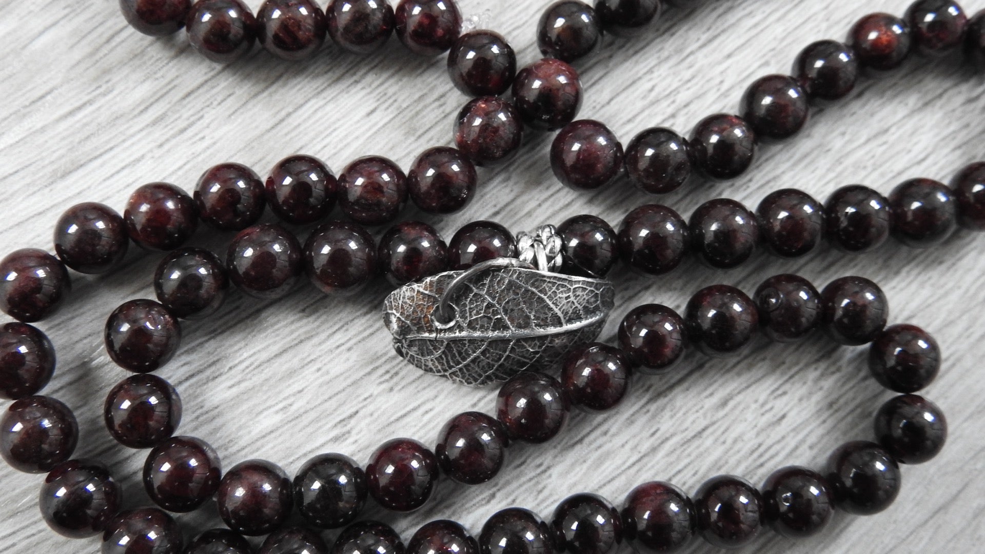 Side profile view of sterling silver leaf pendant showing three-dimensional organic leaf form with garnet accents and antique finish.