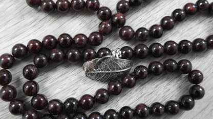 Side profile view of sterling silver leaf pendant showing three-dimensional organic leaf form with garnet accents and antique finish.