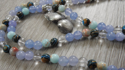 Side profile view of handcrafted sea shell pendant showing three-dimensional sterling silver shell formation with blue stone accents.