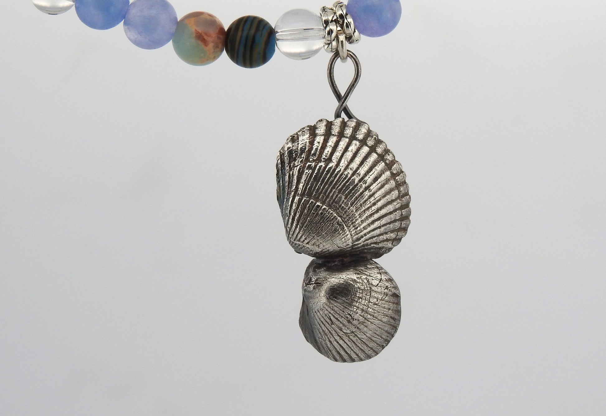 Handcrafted sterling silver sea shell pendant with aquamarine, clear quartz, and blue stones inspired by Northern Ireland coastlines, front view against white background.