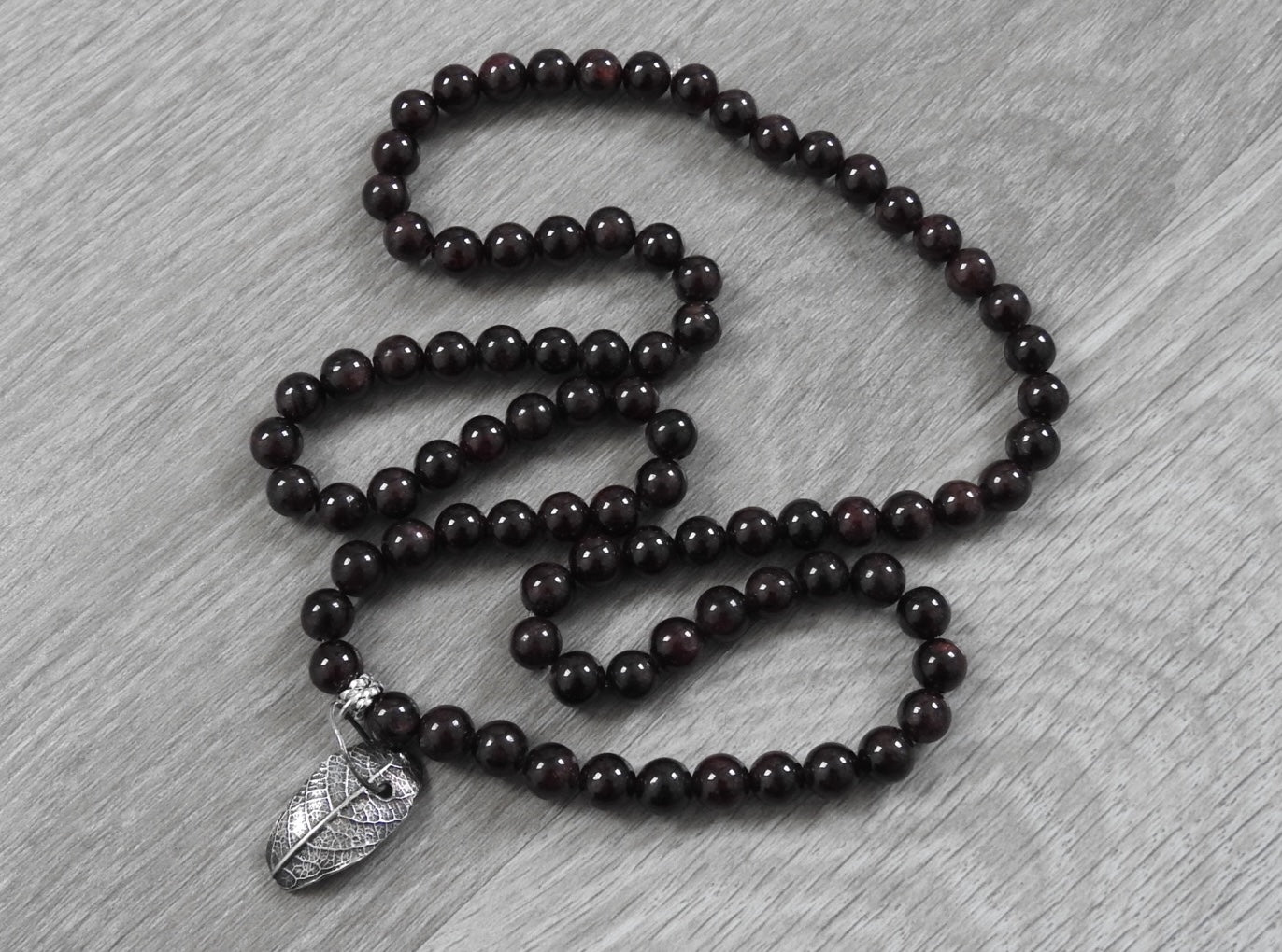 Front view of handcrafted sterling silver leaf pendant with garnet stones showing unique leaf impression and rustic organic design.