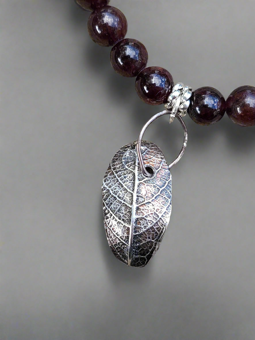Handcrafted sterling silver leaf necklace with garnet stones displayed in natural setting, inspired by Markeaton Park memories in Derby.