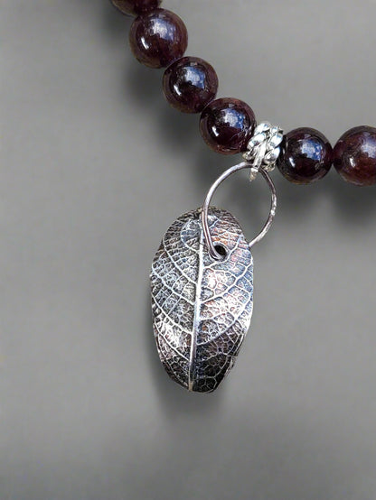 Handcrafted sterling silver leaf necklace with garnet stones displayed in natural setting, inspired by Markeaton Park memories in Derby.
