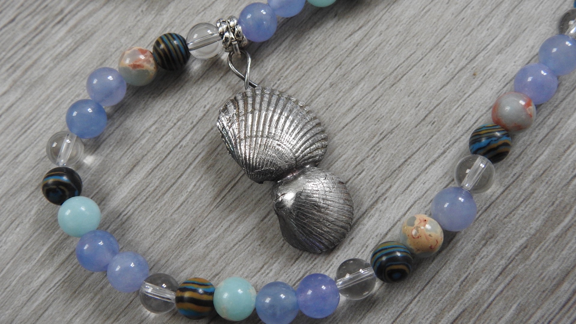Close-up detail of sterling silver sea shell pendant showing aquamarine, clear quartz, blue snakeskin stone, and blue malachite placement.